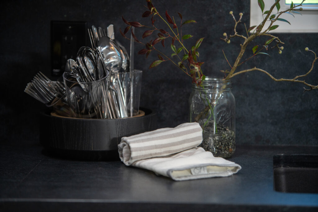 Black countertop with utensils, plant, and towel 