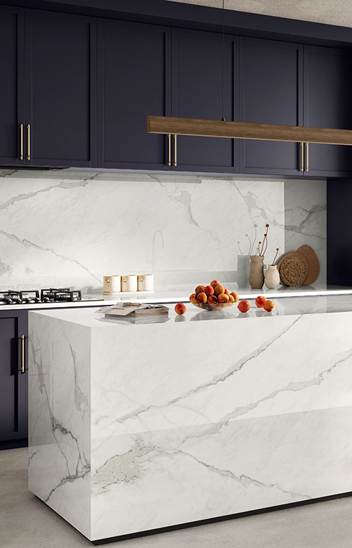 Modern kitchen with marble island, wooden stools, purple cabinets, built-in oven, and gold faucet.