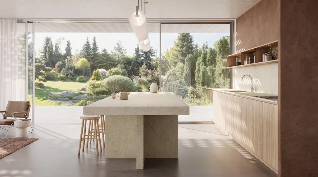 Modern kitchen with large island, bar stools, and floor-to-ceiling windows overlooking greenery.