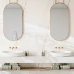 Caesarstone porcelain 502 Sleet surface in Minimalist double vanity with oval mirrors, white vessel sinks, gold faucets, and neatly rolled green towels.