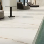 Modern poolside area with cushioned loungers, round sofas, and a small black side table and Caesarstone porcelain 502 Sleet flooring