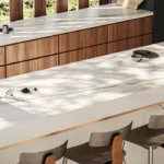Modern kitchen with Caesarstone Porcelain 502 Sleet countertops, wooden cabinetry, black stove, sink, and four bar stools.