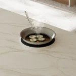 Sliced zucchini frying in a pan on a light-colored kitchen Caesarstone porcelain 506 Mirabel surface countertop.