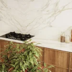 Caesarstone porcelain 506 Mirabel surface in Modern kitchen with marble backsplash, wooden cabinets, gas stove, plant, and cutting board.