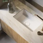 Caesarstone porcelain 506 Mirabel surface in Modern bathroom sink with marble countertop, brass faucet, glass bottle, and soap dispenser.