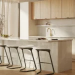 Caesarstone 5110_Alpine Mist in Modern kitchen with a large island, four bar stools, wooden cabinets, and a gold faucet.