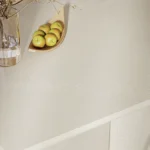 Caesarstone 5110_Alpine Mist surface with Clear glass vase with dried branches, wooden tray holding apples on light-colored countertop.
