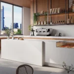 Caesarstone ICON 5112_ATERRA_BLANCA in Modern café interior with large windows, seating, coffee machine, pastries, and city skyline view.