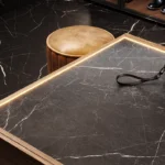 Caesarstone porcelain 511 Smokestone-topped table, leather pouch, round leather ottoman, black marble flooring with white veining, shoes.