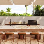Caesarstone Porcelain 536 Antikella surface in Outdoor kitchen with marble island, wooden stools, grill, sink, and tropical greenery background.