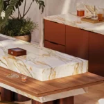 Caesarstone Porcelain 536 Antikella surface in Modern outdoor kitchen with marble countertops, wooden bar stools, plants, and a built-in grill.