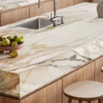 Caesarstone porcelain 536_Antikella surface in a modern kitchen island with wooden stools, a bowl of pears, and decorative vases.