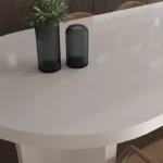White oval Caesarstone 6141 Ocean Foam table with two dark vases and brown chairs around it.