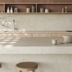 Minimalist kitchen with Caesarstone ICON 8252 Sedara countertops, wooden stools, open shelves, and vase with bare branches.